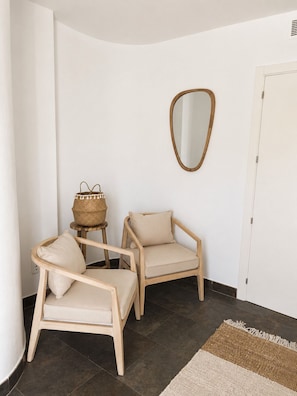 Habitación de esquina con dos sillas de madera, una cesta tejida, un espejo y una alfombra.