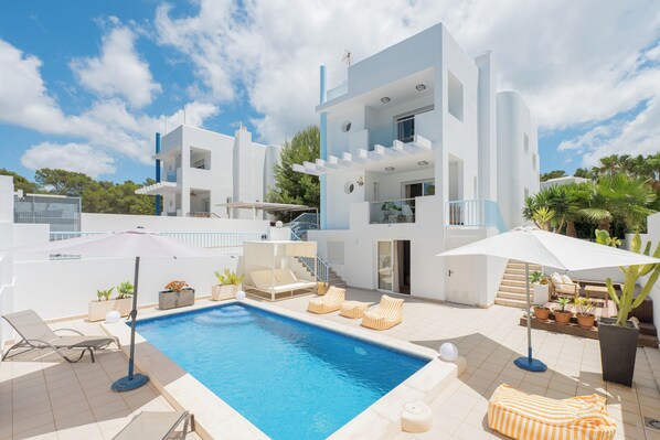 A modern two-story building with a swimming pool, outdoor seating, and potted plants.