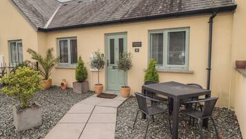 A cottage with a tiled patio, outdoor seating, and potted plants.