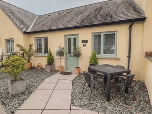 A cottage with a tiled patio, outdoor seating, and potted plants. - Cornstore Cottage (Pembroke)