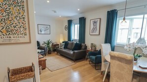 A modern living room with a sofa, armchairs, a coffee table, and a dining area with a chair and table. - Cornstore Cottage (Pembroke)