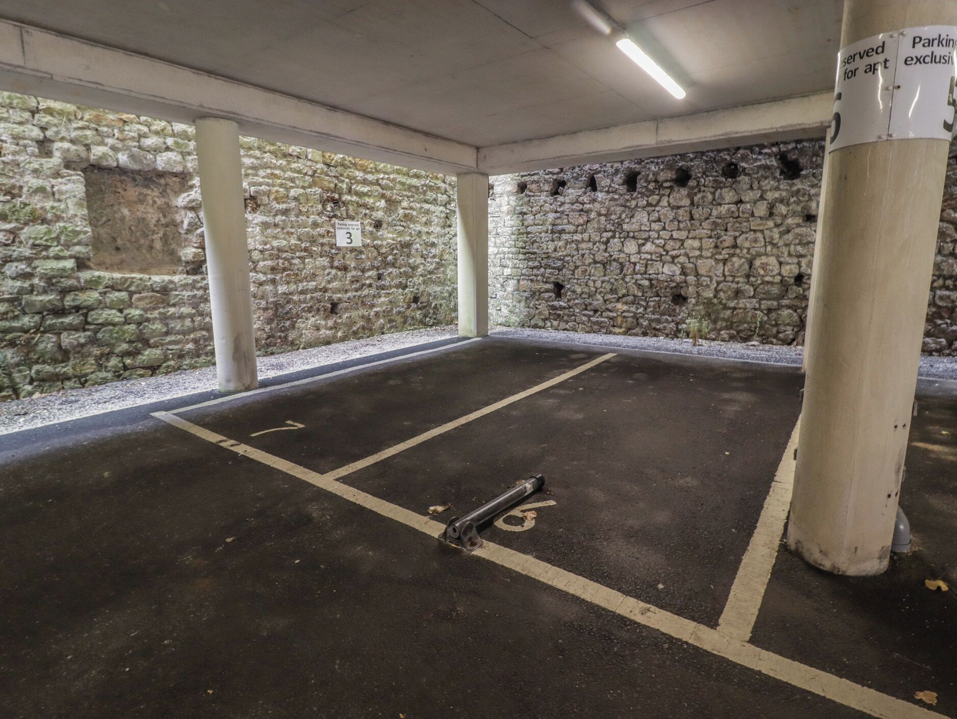 A parking garage with stone walls, concrete pillars, and marked parking spaces.