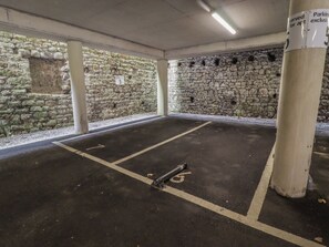A parking garage with stone walls, concrete pillars, and marked parking spaces. - Cornstore Cottage (Pembroke)