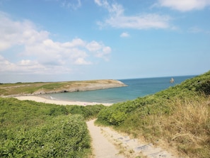 A coastal path leading to a beach with a clear view of the sea and distant rocky outcrops. - Cornstore Cottage (Pembroke)