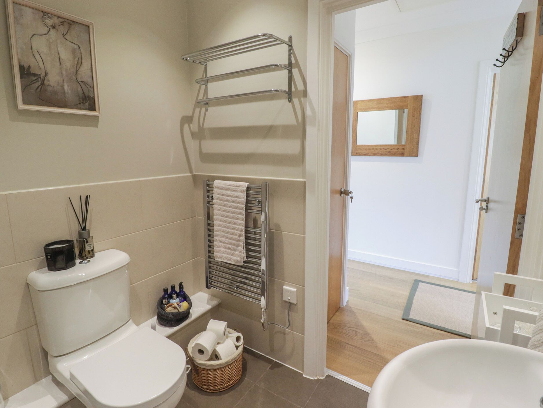 Une salle de bain équipée de toilettes, d’un porte-serviettes, d’un panier contenant du papier toilette et d’une œuvre d’art encadrée accrochée au mur.