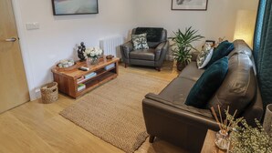 A living room with a sofa, a coffee table, a fireplace, and a painting on the wall. - Cornstore Cottage (Pembroke)