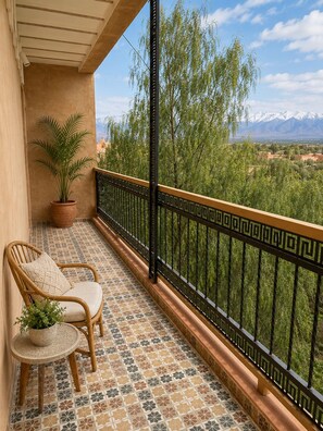 Un balcon doté d  ’un sol à motifs, d’une plante en pot, d’une chaise en osier et offrant une vue sur les montagnes.