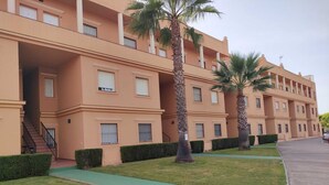 Un hotel de varios pisos con fachada uniforme, un sendero verde y palmeras.