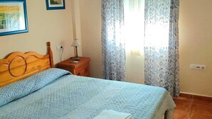Un dormitorio con cama, ventilador de techo, mesita de noche y ventana con cortinas estampadas.