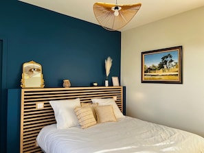 Ein Schlafzimmer mit Bett, Kopfteil, einem an der Wand befestigten Bild und einer Pendelleuchte.