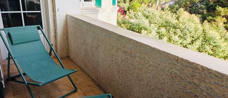 Un balcon avec deux fauteuils de jardin verts, un mur blanc et une vue sur un jardin et des maisons.