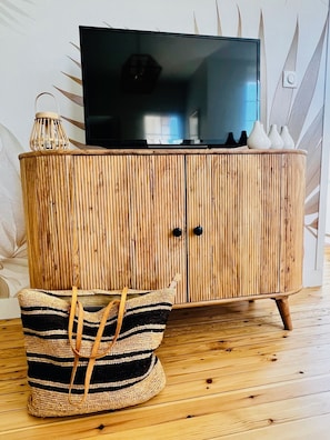 Ein Holzschrank mit einem Fernseher darauf, ein gewebter Korb und dekorative Vasen.
