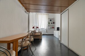 Ein Essbereich mit einem Holztisch und Stühlen, einer Couch, einem Fenster mit Vorhängen und einer weißen Schrank mit Regalen.