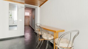 Un corridoio con soffitto in legno, parete bianca, uno specchio, un tavolo di legno con quattro sedie e una porta che dà su un'altra stanza.
