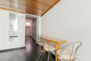Ein Flur mit Holzboden, einer weißen Wand, einem Spiegel, einem Holztisch mit vier Stühlen und einer Tür zu einem anderen Raum.