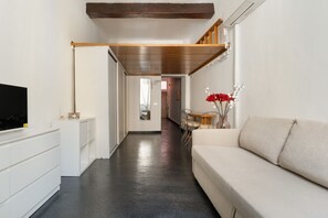 Ein modernes Wohnzimmer mit Sofa, Fernseher, Essbereich und einem Flur, der in einen weiteren Raum führt.