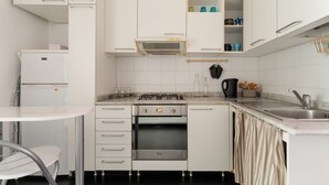 Una cucina compatta con mobili bianchi, forno integrato, piano cottura a gas e piccolo frigorifero.