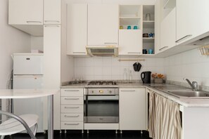 Eine kleine Küche mit weißen Schränken, einem eingebauten Ofen, einem Gasherd und einem kleinen Kühlschrank.