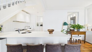 A modern kitchen with a large island, white cabinetry, and a dining area with a wooden table and chairs. - Family Home with Rooftop Terrace in Notting Hill sleeps 5 (London)