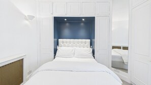 Ein Schlafzimmer mit einem weißen Bett, einer blauen Akzentwand, weißen Schränken und einer Deckenleuchte.