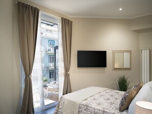 Ein Schlafzimmer mit einem Bett, einem Fernseher, einem Spiegel und Blick auf einen Balkon.