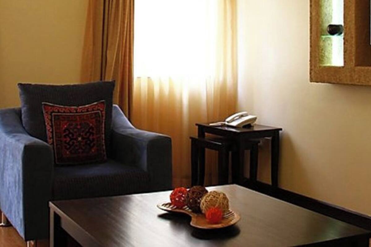 Una habitación con un sillón azul, una mesa de centro de madera con objetos decorativos, una mesita con un teléfono y un televisor montado en la pared.