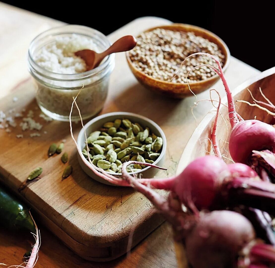 A wooden cutting board with a bowl of seeds, a jar of a white substance, and a radish.