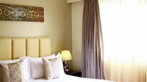A hotel room with a bed, pillows, a lamp, a curtain, and a wall art piece. - Reata Apartment Hotel (Nairobi)