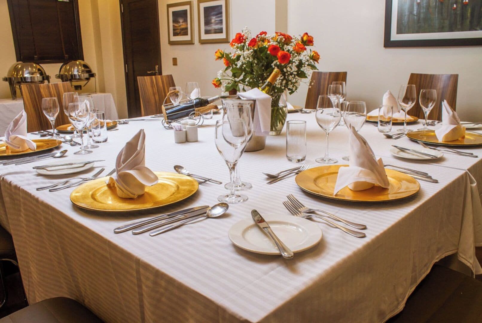 A table set for a formal dinner with gold plates, silverware, and a centerpiece of flowers.