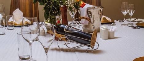 Una mesa de comedor dispuesta con copas de vino, cubiertos y un centro de mesa decorativo.