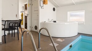 Et moderne poolområde indendørs med et boblebad, et opholdsområde med stole og et vindue med naturligt lys.