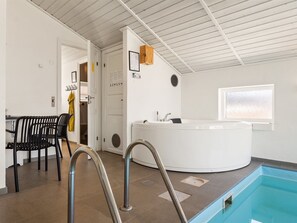 Ein moderner Poolbereich im Innenbereich mit Whirlpool, einer Sitzecke mit Stühlen und einem Fenster, das für natürliches Licht sorgt.