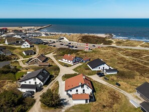 Ein Luftbild eines Küstdorfes mit Häusern, einem Leuchtturm und einem Strand.