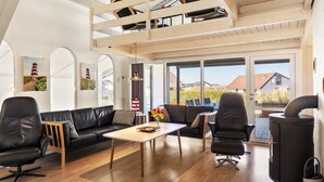 Et moderne interiør med loft-stil loft, en sort lædersofa, et spisebord og en brændeovn.