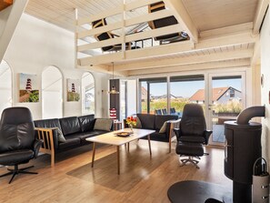 Ein modernes Interieur mit einer Loft-Decke, einem schwarzen Ledersofa, einem Esstisch und einem Kaminofen.