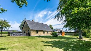 Ein Haus mit geneigtem Dach, einem eingezäunten Garten und Bäumen.