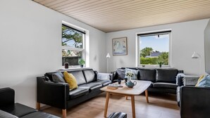 Ein modernes Wohnzimmer mit zwei schwarzen Ledersofas, einem Holztisch und großen Fenstern, die für natürliches Licht sorgen.