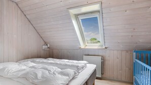 Ein Schlafzimmer mit Schräge, einem Fenster, einer Heizung und einem blauen Babybett.