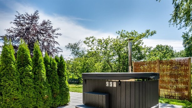 Ein moderner Whirlpool im Freien mit Holzkonstruktion, umgeben von einer gepflasterten Terrasse und üppiger Vegetation.