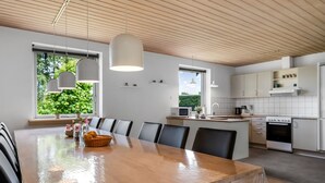 Eine moderne Küche mit Holzboden, weißen Schränken und einem Essbereich mit großem Tisch und Stühlen.