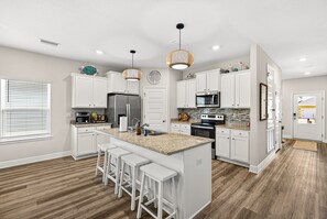 A modern kitchen with white cabinetry, a central island with stools, a microwave, refrigerator, and a sink.