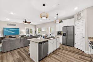 A modern kitchen with a central island, stainless steel appliances, and a large flat-screen TV.