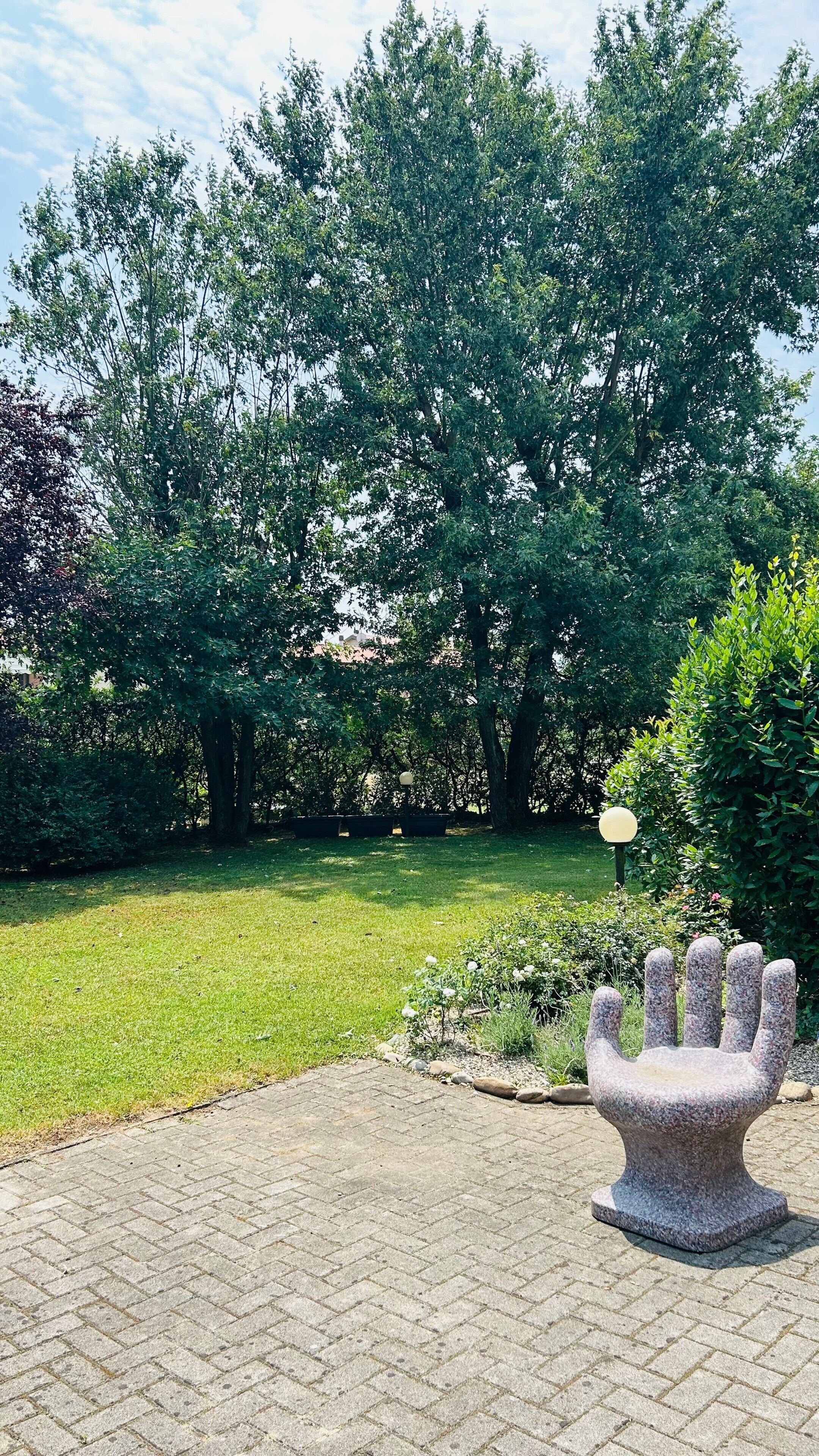 Een geplaveid gebied met een stenen sculptuur, omringd door gras en bomen.