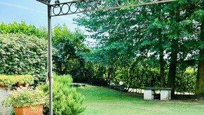 An outdoor patio with a table covered in a blue patterned tablecloth, surrounded by chairs, under a yellow canopy. - Garden House, a Quiet Retreat Just 30 Minutes from Milan (Pavia)