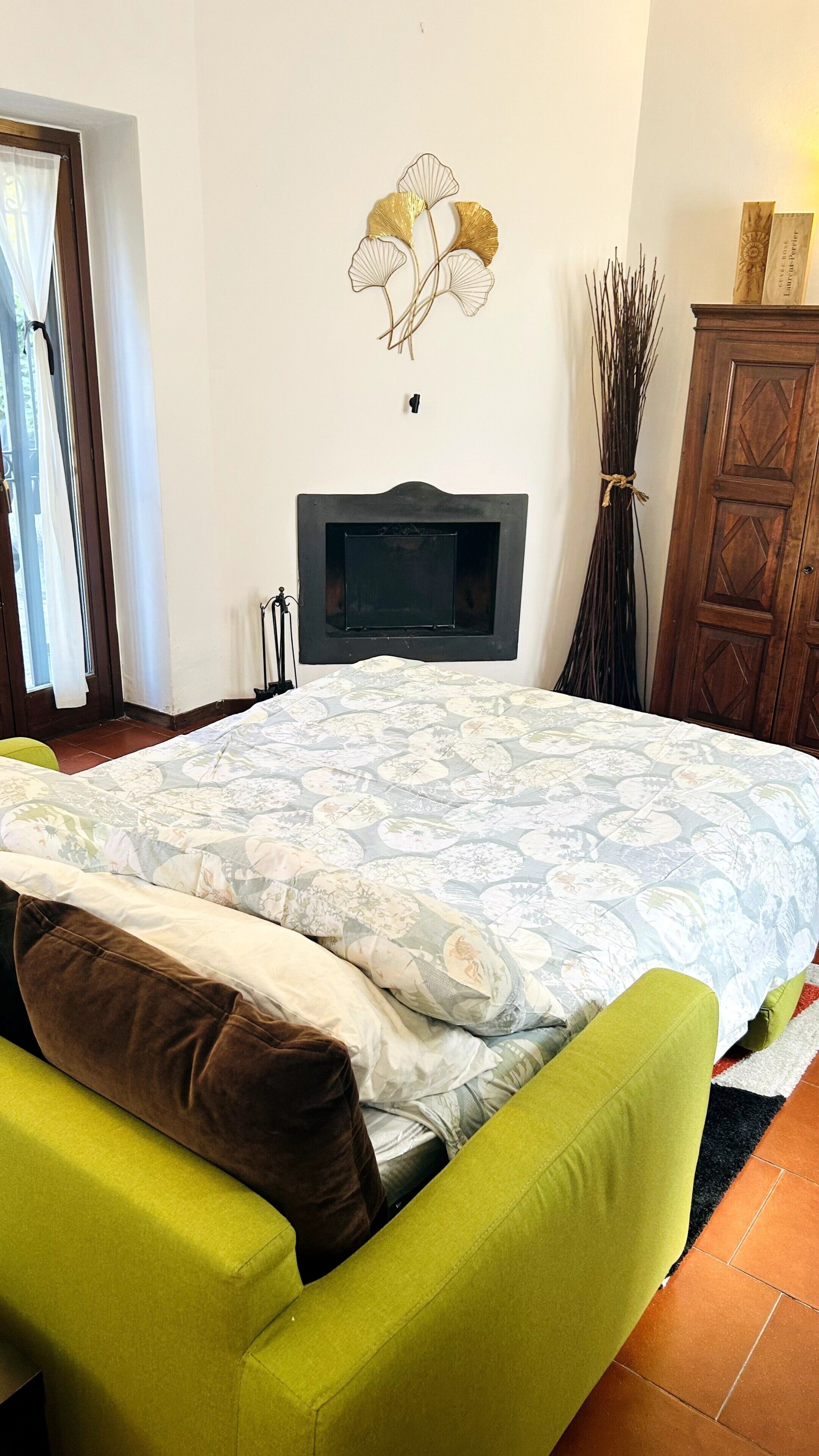 A bedroom with a bed, green armchair, fireplace, and decorative wall art.