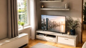 Una sala de estar moderna con una televisión de pantalla plana, un radiador, una ventana con cortinas, un tapete gris y un sofá.