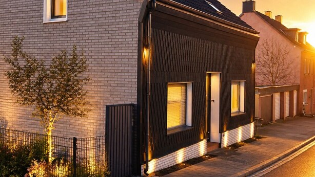 Un edificio residencial moderno con fachada de ladrillo, un añadido de madera oscura y un ventanal visible.