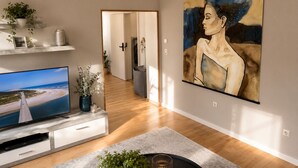 Una sala de estar moderna con un televisor de pantalla plana, un cuadro abstracto grande y un pasillo que conduce a otra habitación.