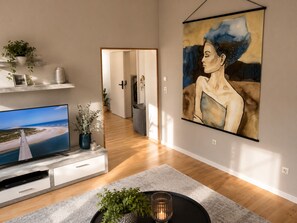 Ein modernes Wohnzimmer mit einem Flachbildfernseher, einem großen abstrakten Gemälde und einem Flur zu einem weiteren Raum.