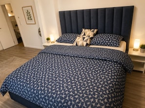 A bedroom with a bed, two bedside tables, a nightstand, a rug, and a framed picture on the wall.
